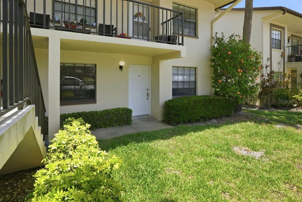 A ground-level apartment entrance with a white door, a small patio, and a balcony above — 2400 WINDING CREEK BOULEVARD UNIT 20A-109, CLEARWATER, FL