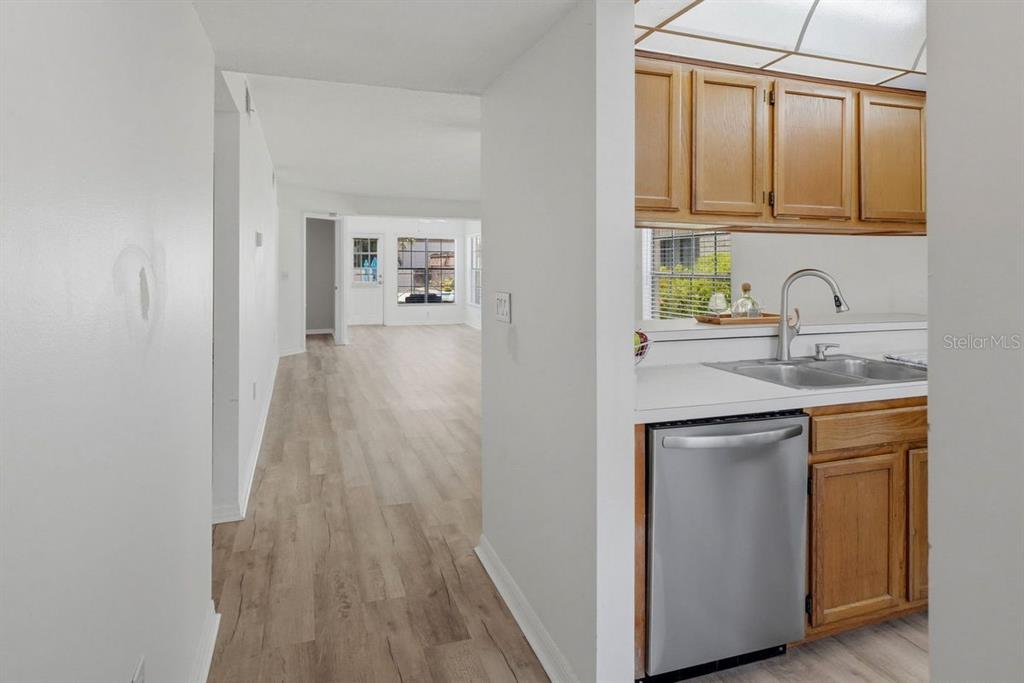 A view from a kitchen with wood cabinets toward an open living area with flooring — 2400 WINDING CREEK BOULEVARD UNIT 20A-109, CLEARWATER, FL