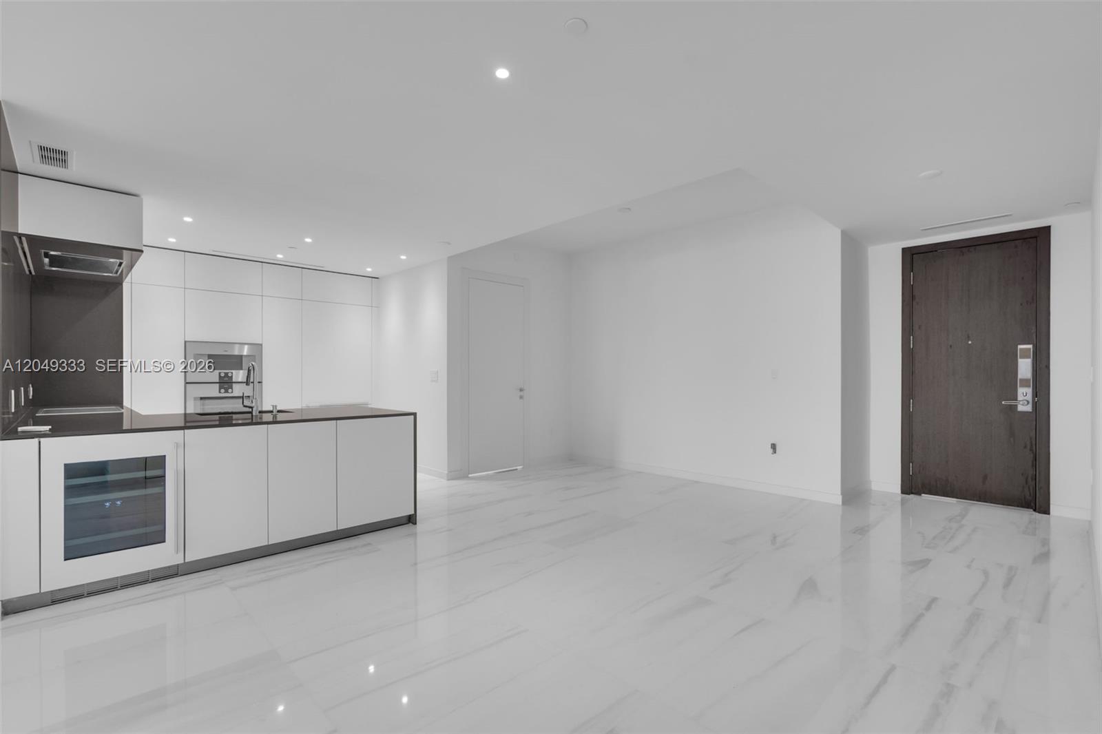 A modern kitchen with white cabinetry and marble flooring opens into an empty living area — 300 Biscayne Boulevard Way # 3009W, Miami FL 33131, MIAMI, FL