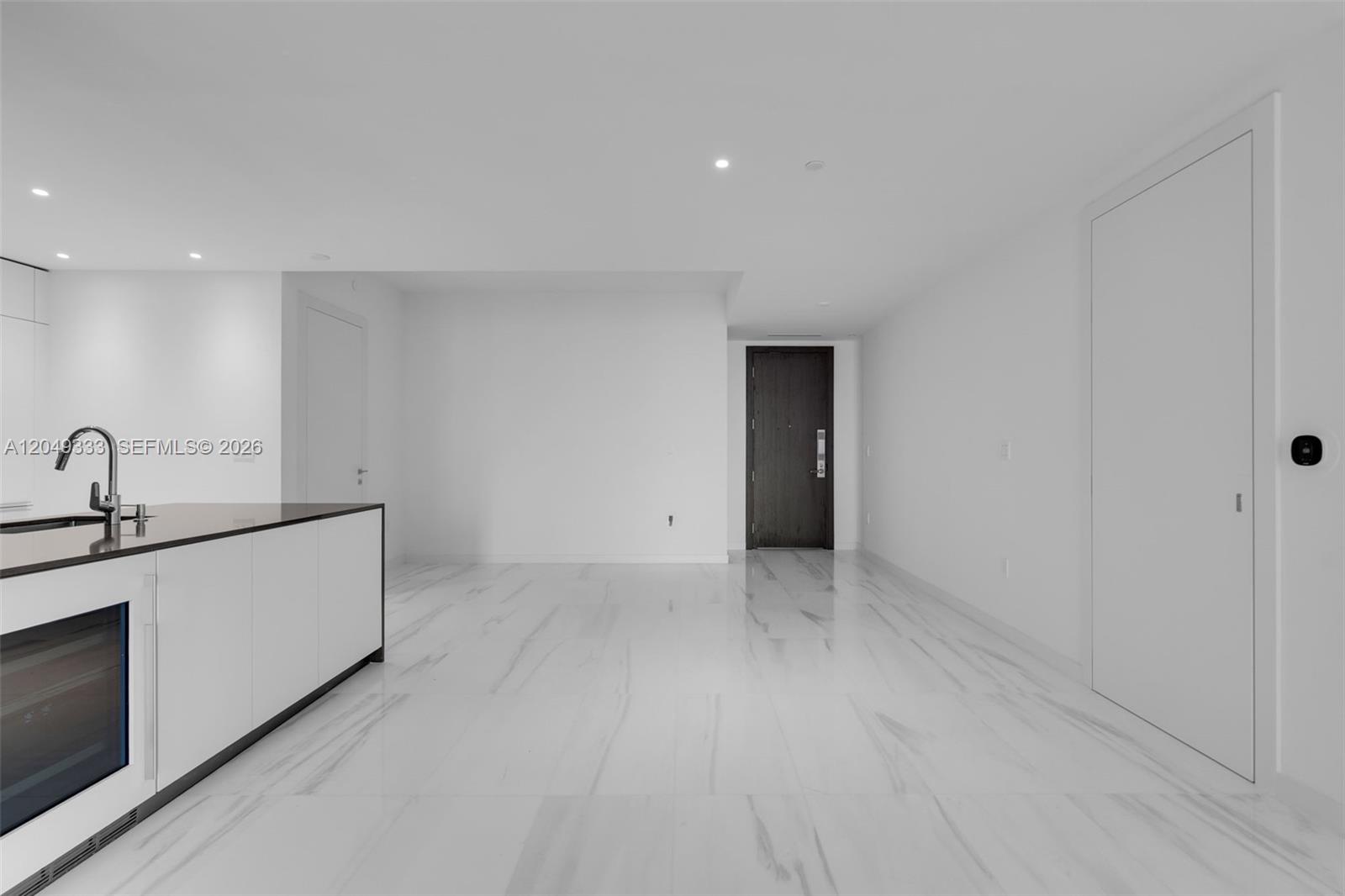 A modern, minimalist kitchen area features white cabinetry, a dark countertop, and white marble flooring — 300 Biscayne Boulevard Way # 3009W, Miami FL 33131, MIAMI, FL