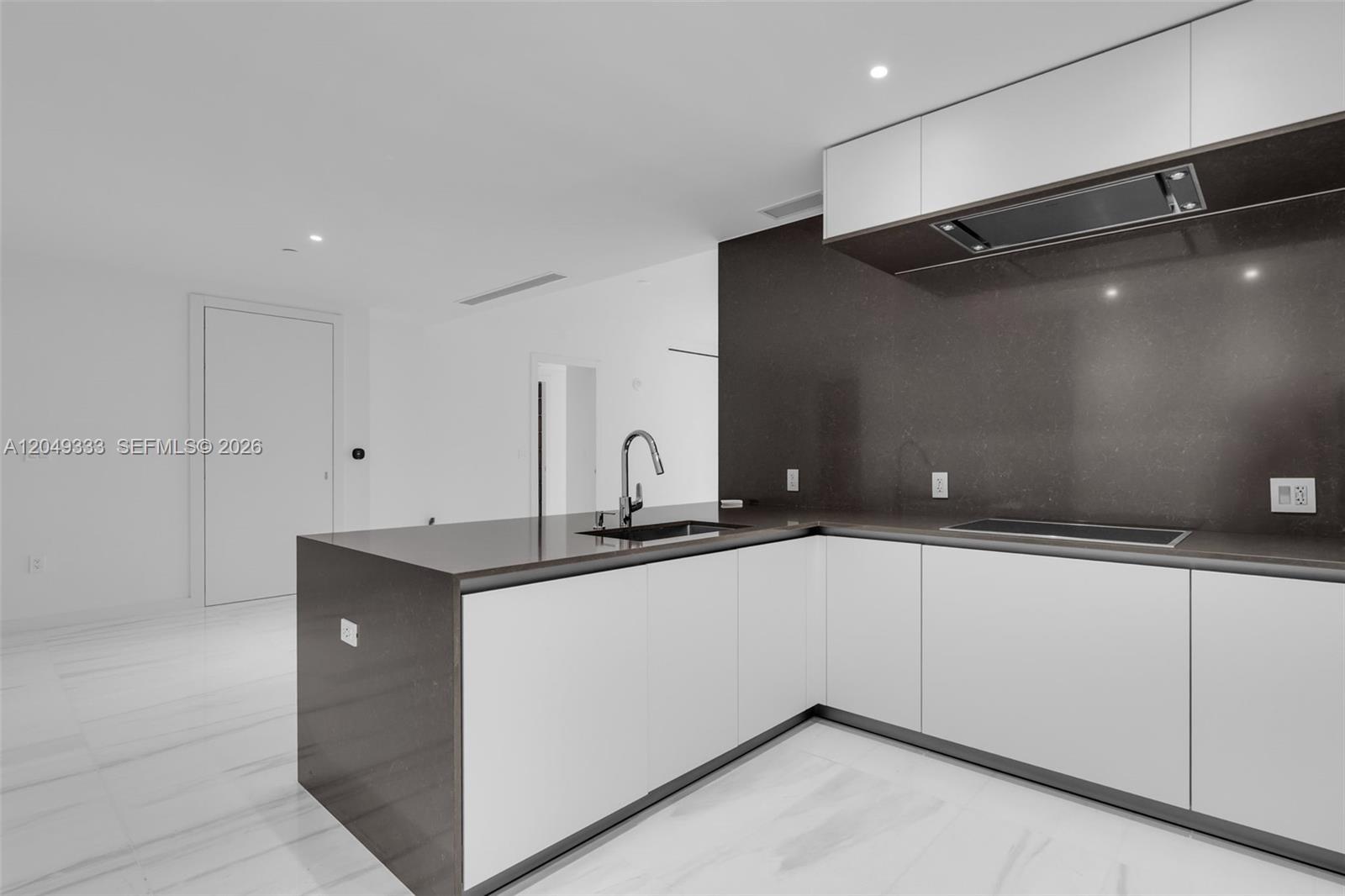 A modern kitchen features white cabinets, dark countertops, and a stainless steel sink — 300 Biscayne Boulevard Way # 3009W, Miami FL 33131, MIAMI, FL
