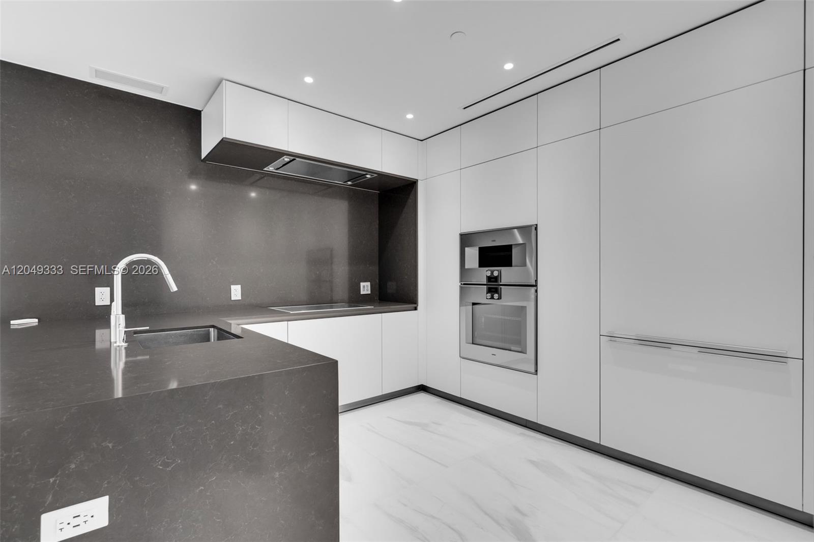 A modern kitchen features dark gray countertops, white cabinetry, and stainless steel built-in appliances — 300 Biscayne Boulevard Way # 3009W, Miami FL 33131, MIAMI, FL