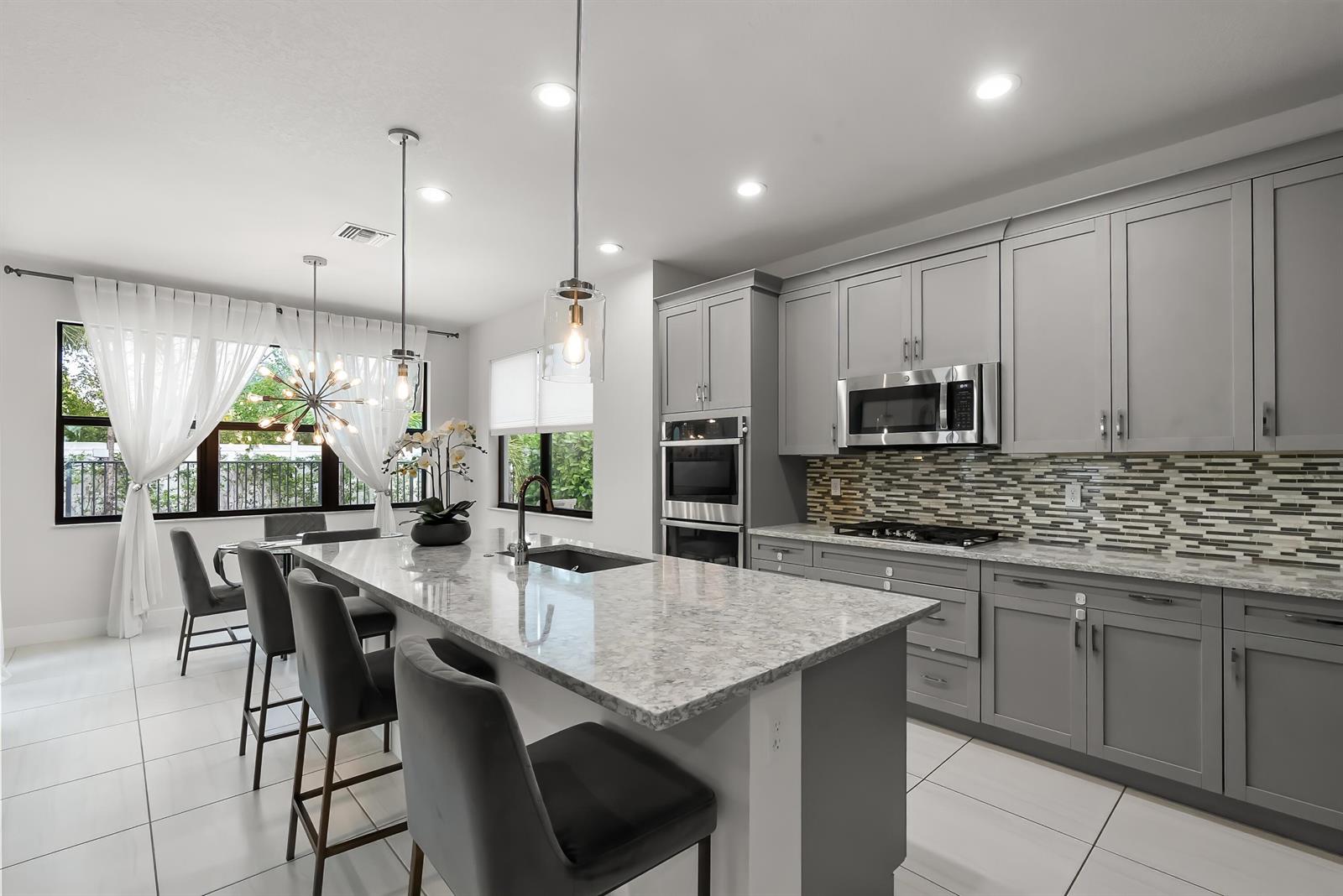 A modern kitchen features gray cabinets, a large granite island, and stainless steel appliances — 7241 Stella Lane, Lake Worth FL 33463, LAKE WORTH, FL