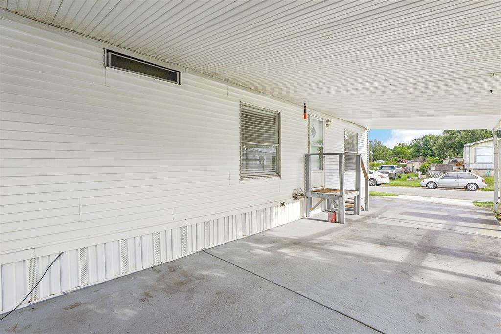 A white mobile home exterior features a concrete carport and a small wooden porch — 2638 SEA OATS CIRCLE S, LAKELAND, FL