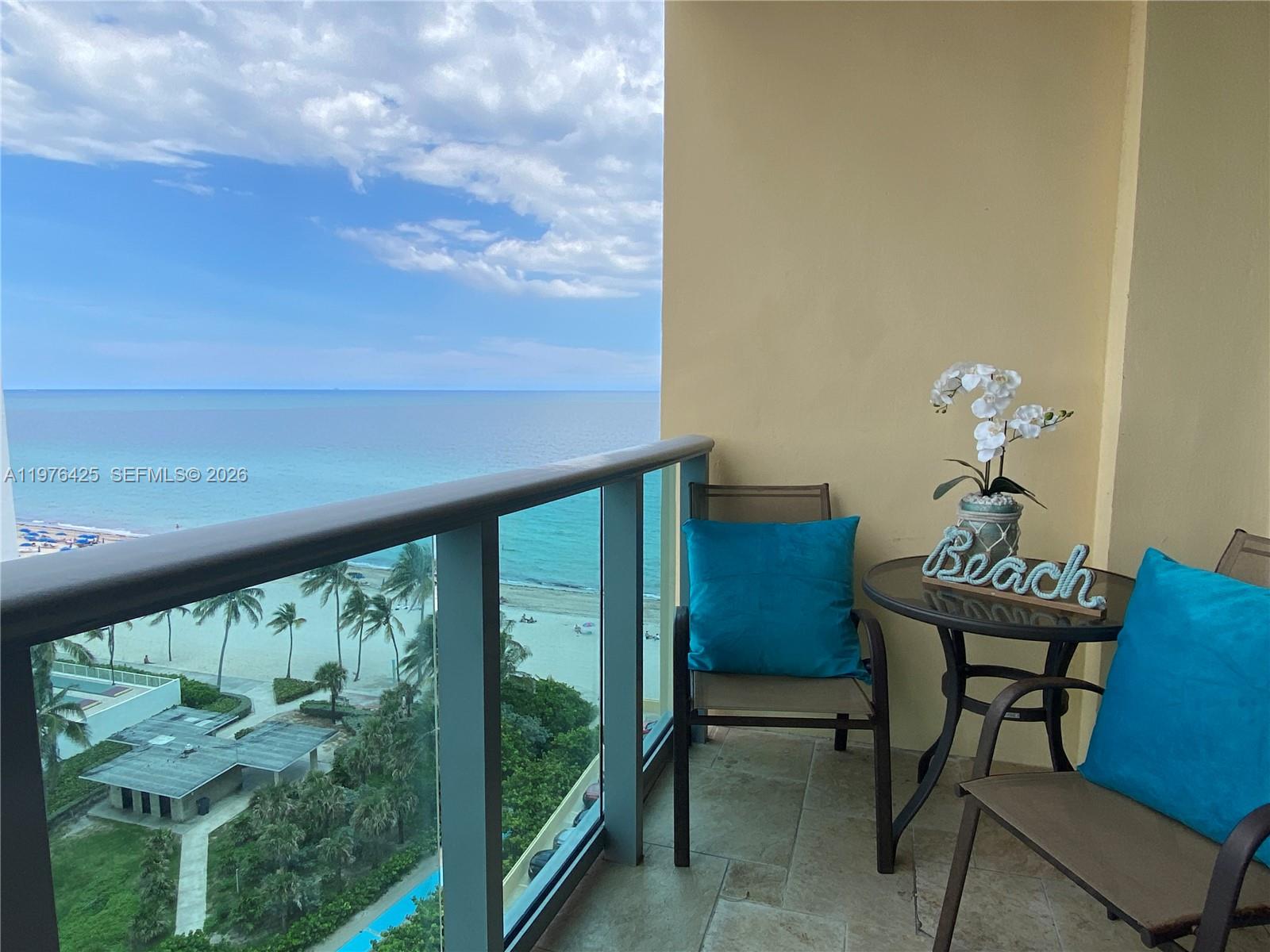 A balcony features two chairs with blue pillows, a small table, and an ocean view — 2501 S Ocean Dr # 1104, Hollywood FL 33019, HOLLYWOOD, FL