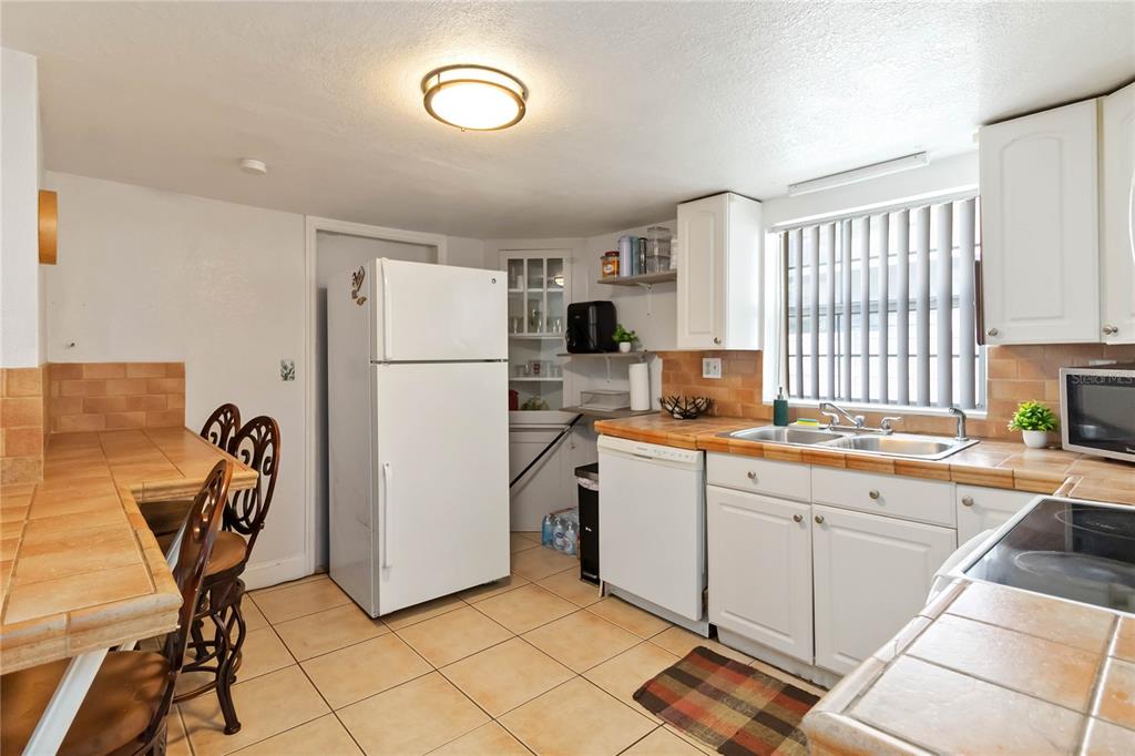 A kitchen features white cabinets, tile countertops, a white refrigerator, and a dishwasher — 710 BAY STREET, KISSIMMEE, FL