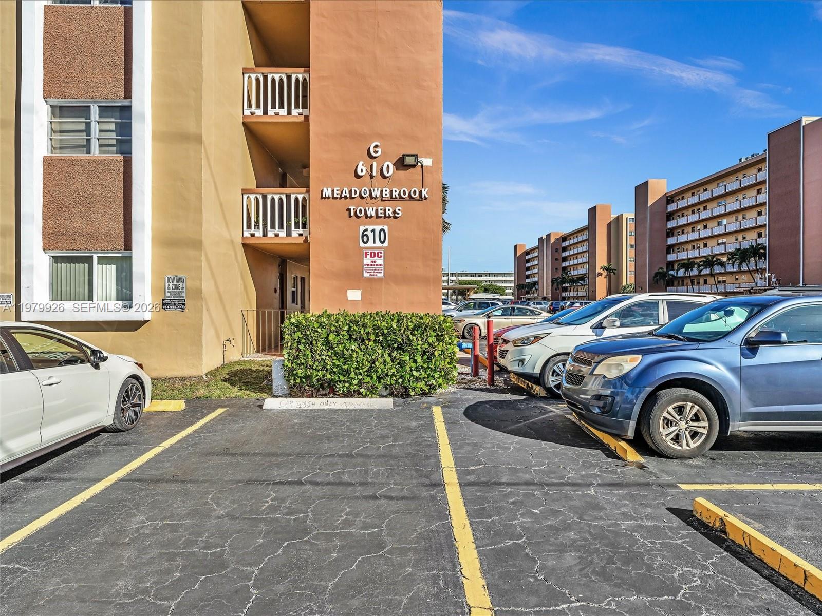 The exterior of a multi-story apartment building features a parking lot with several parked cars — 610 NE 12th Ave # 203, Hallandale Beach FL 33009, HALLANDALE BEACH, FL