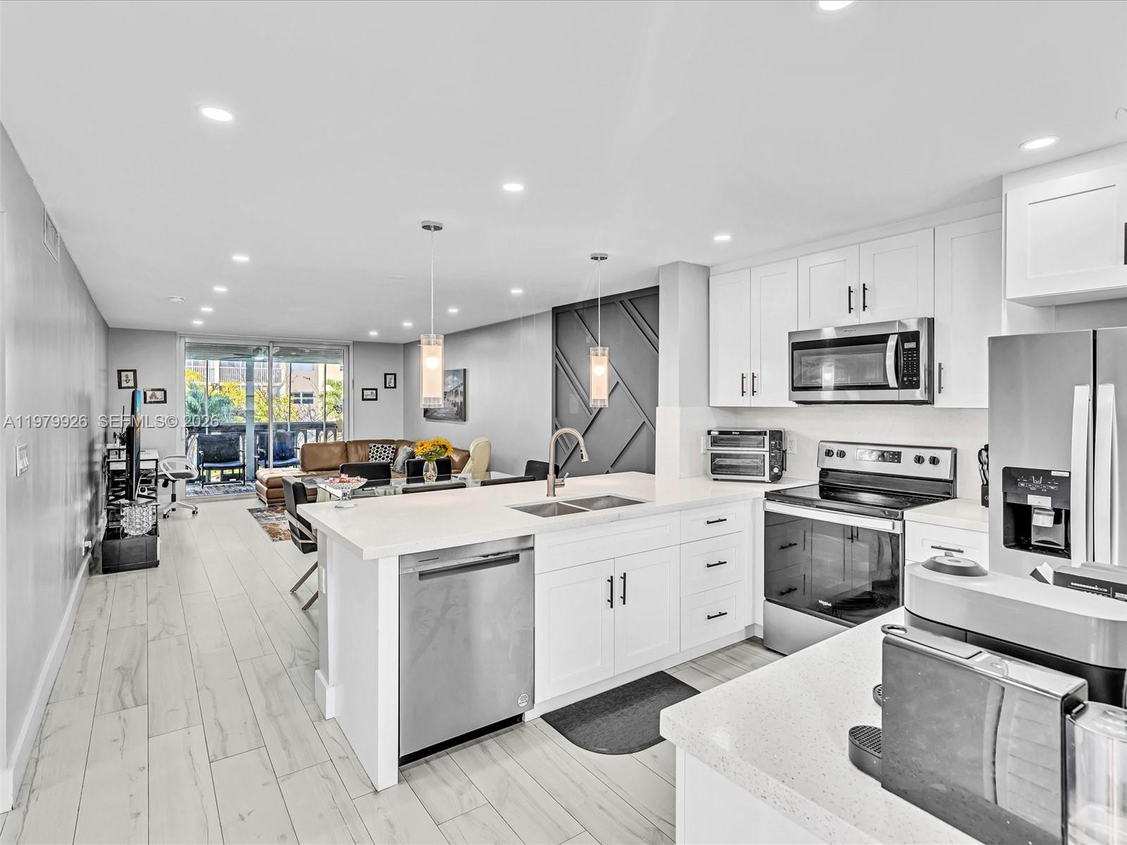 A modern kitchen with white cabinetry and quartz countertops opens into a bright living area — 610 NE 12th Ave # 203, Hallandale Beach FL 33009, HALLANDALE BEACH, FL