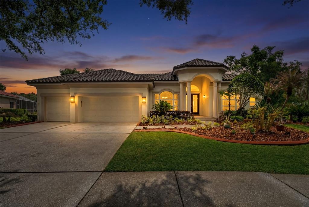 A single-story house with a tile roof, three-car garage, and arched entryway at dusk — 17905 ARBOR GREENE DRIVE, TAMPA, FL
