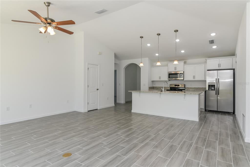 A bright, open-concept kitchen and living area featuring gray wood-look tile flooring and white cabinetry — 1251 AMAZON LANE, KISSIMMEE, FL