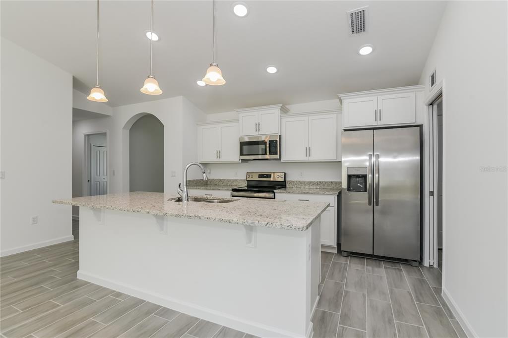 A kitchen with white cabinets, granite countertops, stainless steel appliances, and gray tile flooring — 1251 AMAZON LANE, KISSIMMEE, FL