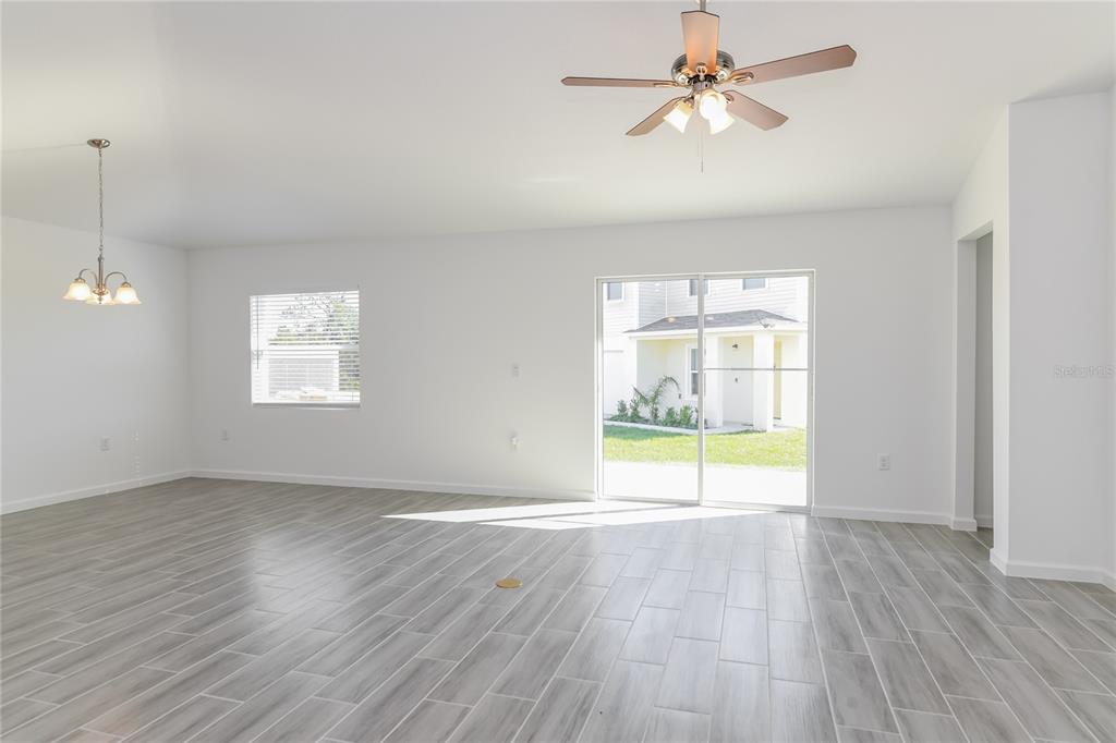 A bright, open-concept living area features light wood-look tile flooring, a ceiling fan, and sliding doors — 1251 AMAZON LANE, KISSIMMEE, FL