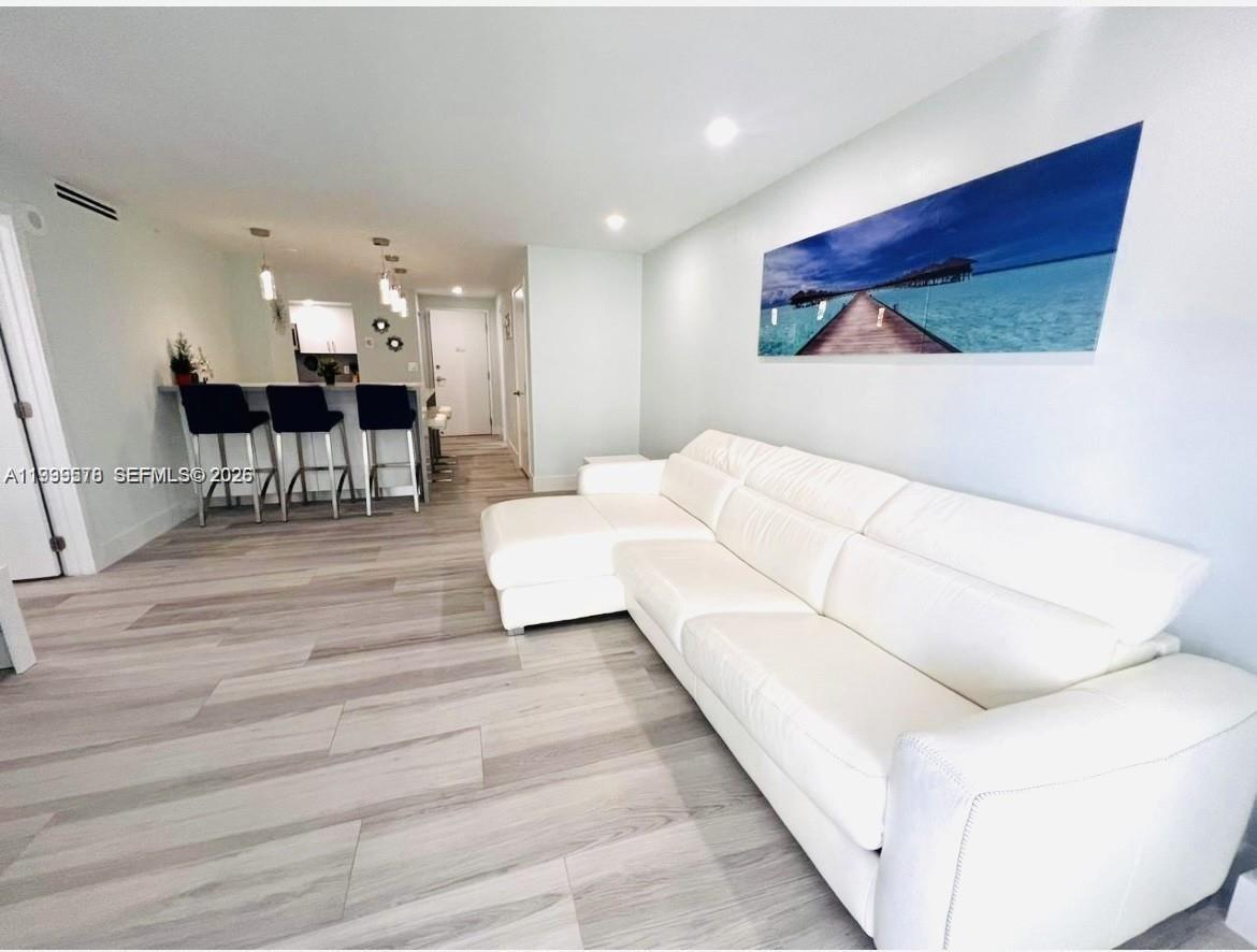 A white sectional sofa sits in a living room with light wood-look flooring and a kitchen — 6917 Collins Ave # 806, Miami Beach FL 33141, MIAMI BEACH, FL
