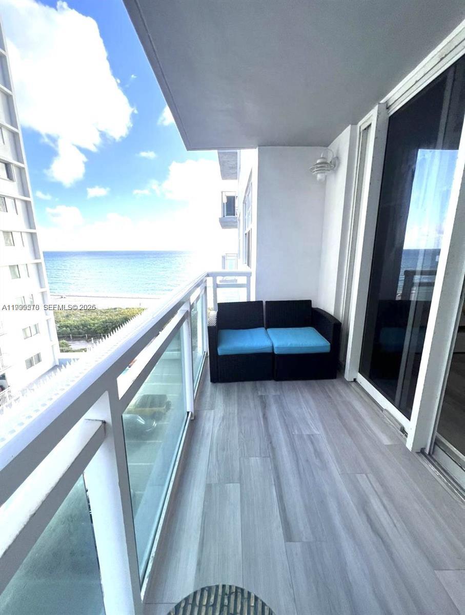 A balcony with gray wood-look flooring, a black wicker loveseat, and an ocean view — 6917 Collins Ave # 806, Miami Beach FL 33141, MIAMI BEACH, FL