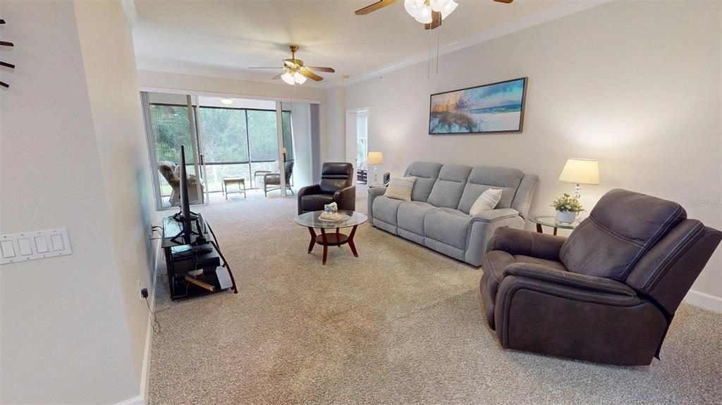 A living room features carpeted floors, a gray sofa, two recliners, and a screened-in patio — 7434 BOTANICA PARKWAY UNIT 101, SARASOTA, FL