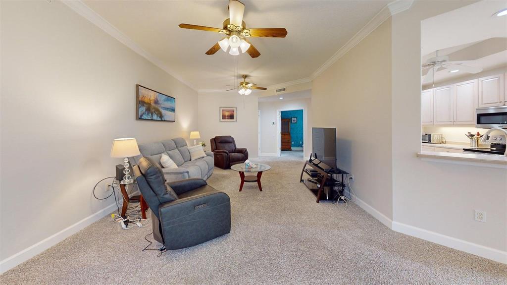 A living room with carpeted floors, a gray sofa, two recliners, and an open kitchen — 7434 BOTANICA PARKWAY UNIT 101, SARASOTA, FL