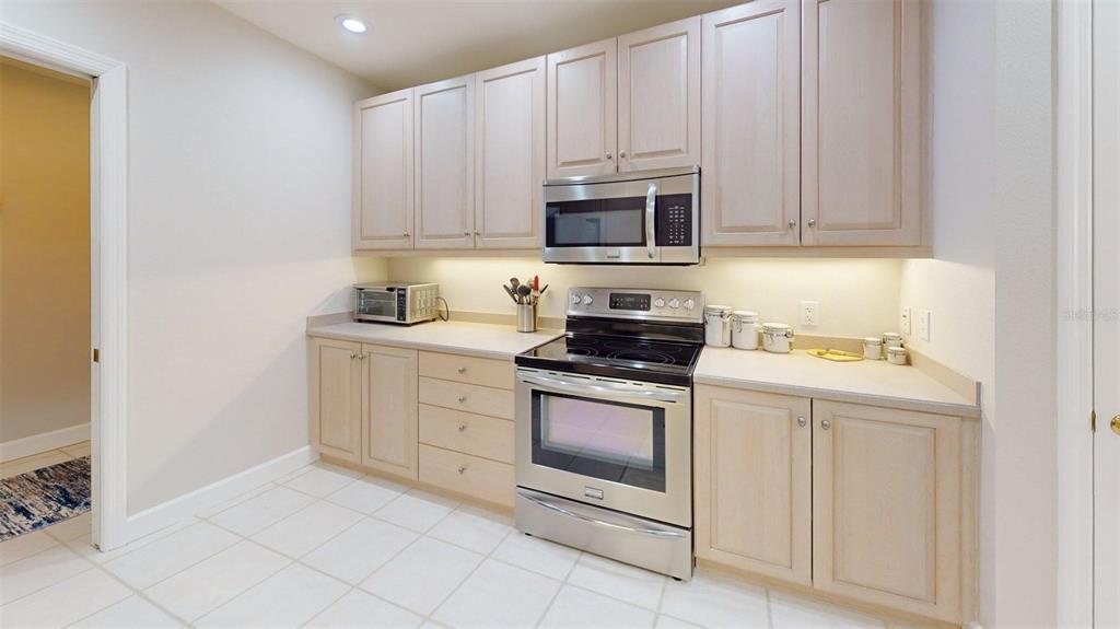 A kitchen features light wood cabinets, stainless steel appliances, and beige tile flooring — 7434 BOTANICA PARKWAY UNIT 101, SARASOTA, FL