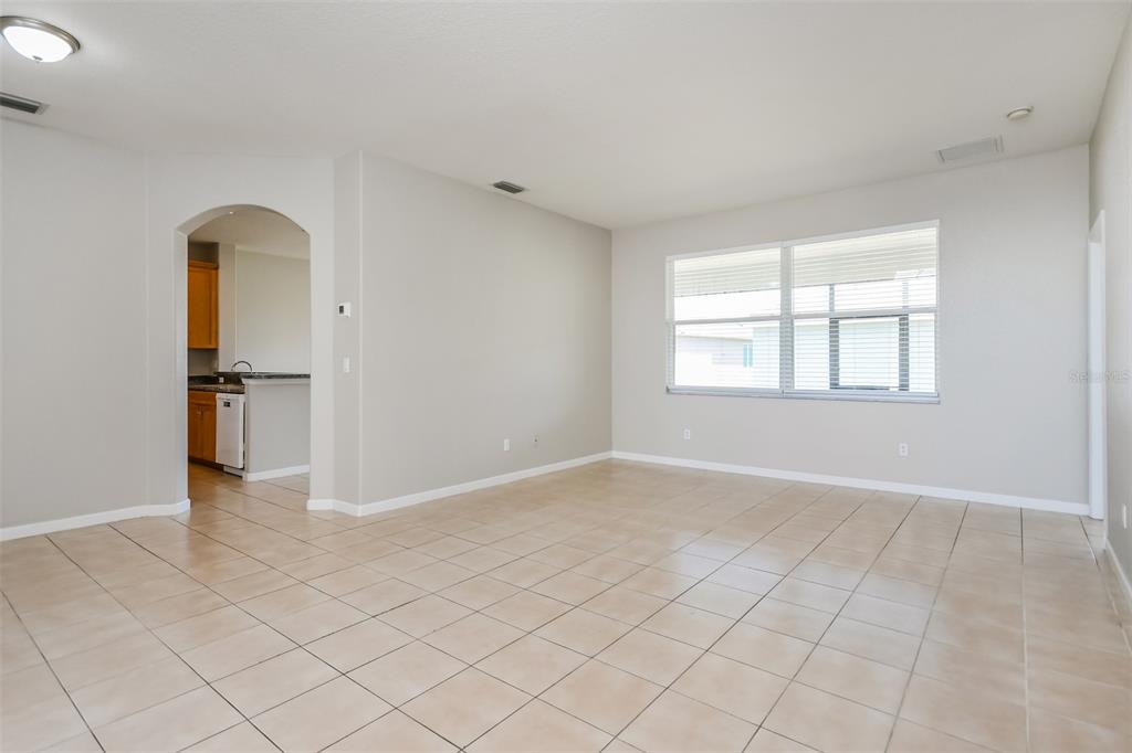 An empty living room with beige tile flooring, light gray walls, and a large window — 2925 WILLOW CREEK LANE, KISSIMMEE, FL