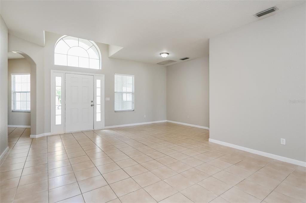 A bright, empty living room features light tile flooring, neutral walls, and a front entryway — 2925 WILLOW CREEK LANE, KISSIMMEE, FL