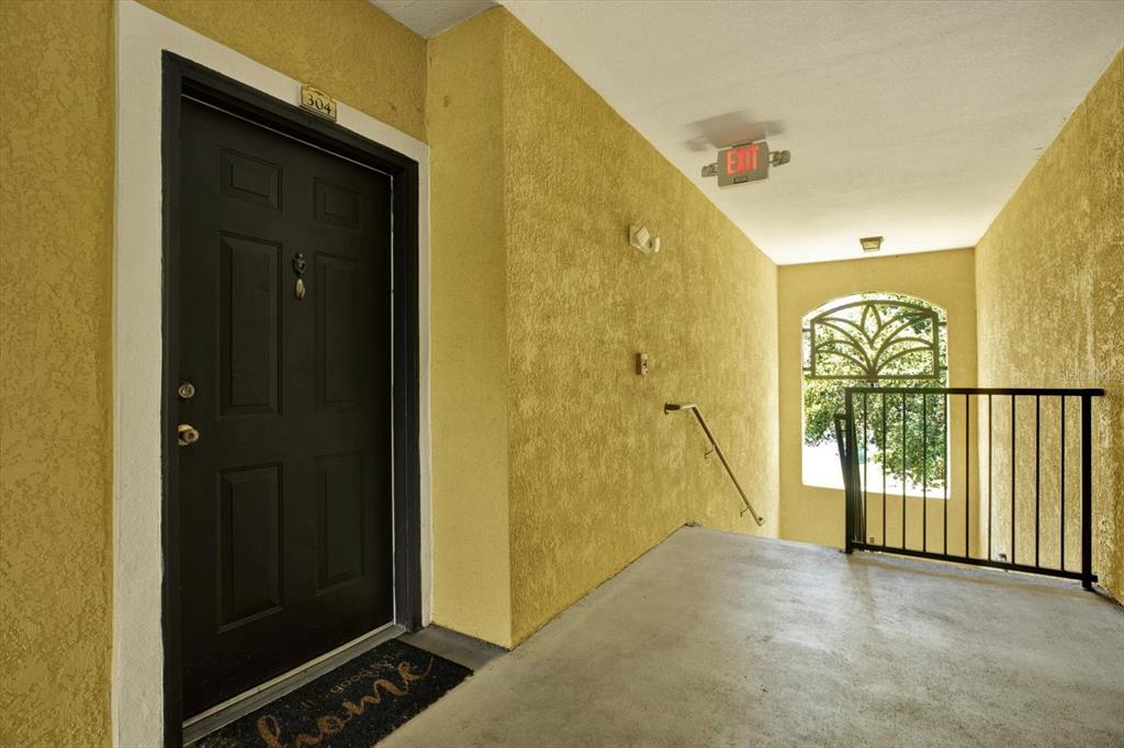 An apartment entrance with a black door, yellow textured walls, and a metal stair railing — 10201 COURTNEY PALMS BOULEVARD UNIT 304, TAMPA, FL