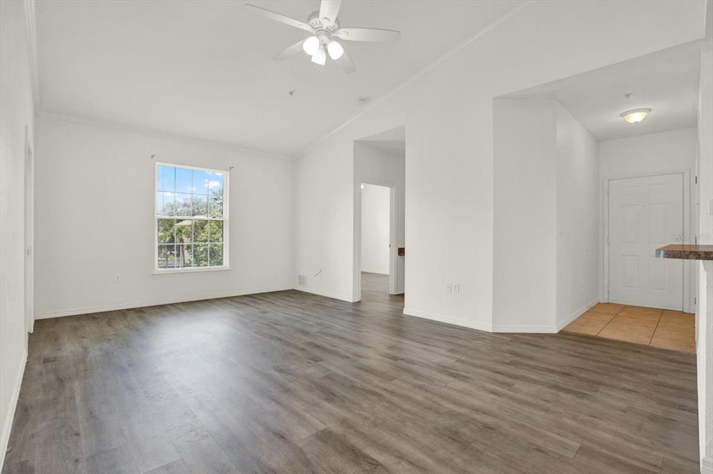 An empty living room with white walls, wood-look flooring, a ceiling fan, and a window — 10201 COURTNEY PALMS BOULEVARD UNIT 304, TAMPA, FL