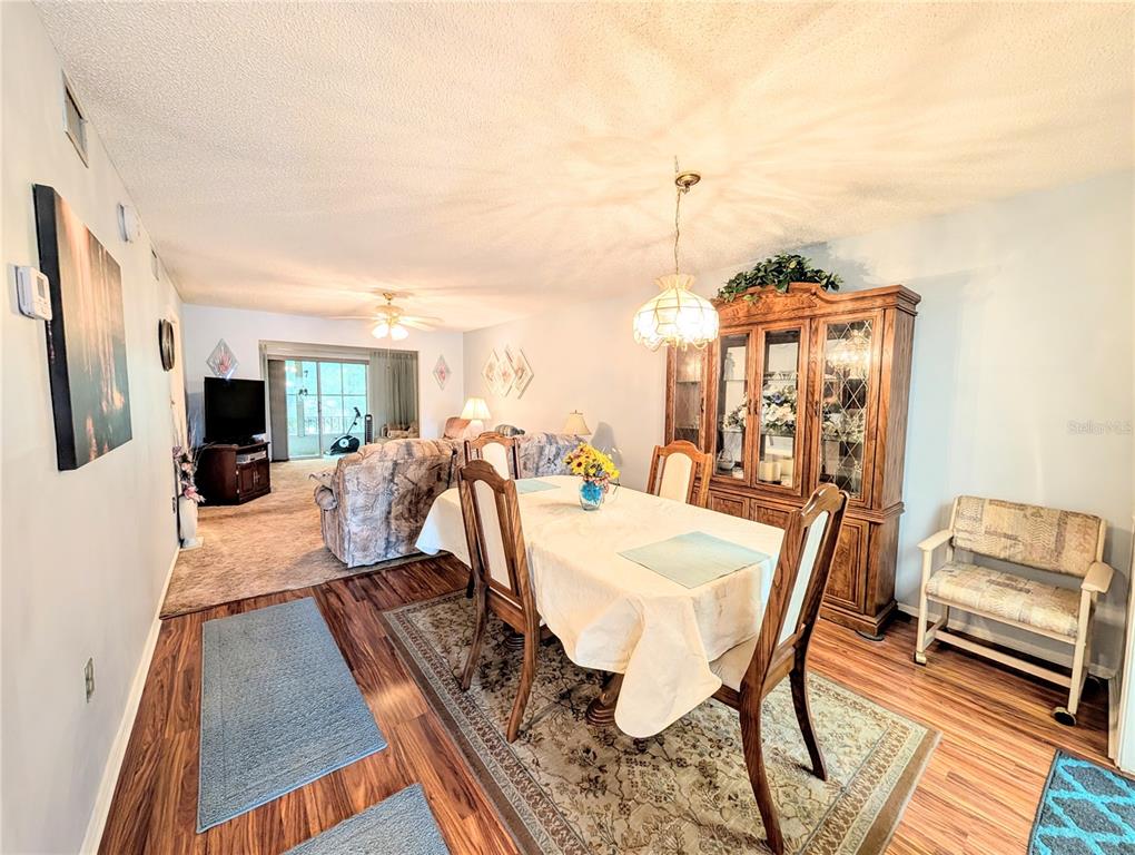 A dining area with a wood-finish hutch and table leads into a carpeted living room — 3624 LAKE BAYSHORE DRIVE UNIT K-303, BRADENTON, FL