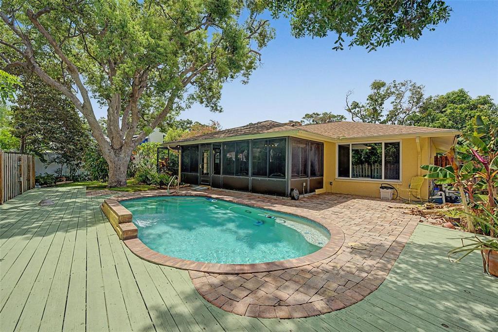 A backyard features a swimming pool, a paved patio, and a wooden deck under trees — 1100 PERSIMMON DRIVE, PALM HARBOR, FL