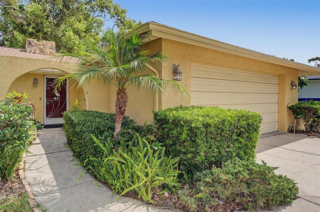 A yellow house exterior features a garage, a palm tree, and a covered front entrance — 1100 PERSIMMON DRIVE, PALM HARBOR, FL