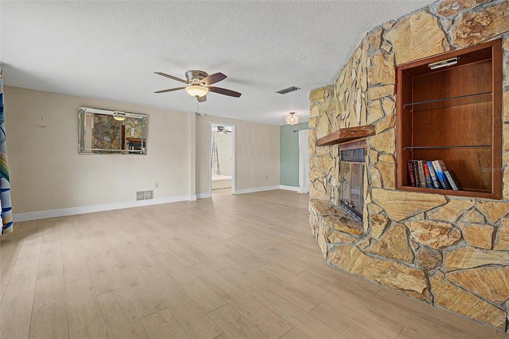 A living room features light wood-look flooring, a stone fireplace, and a built-in bookshelf — 1100 PERSIMMON DRIVE, PALM HARBOR, FL