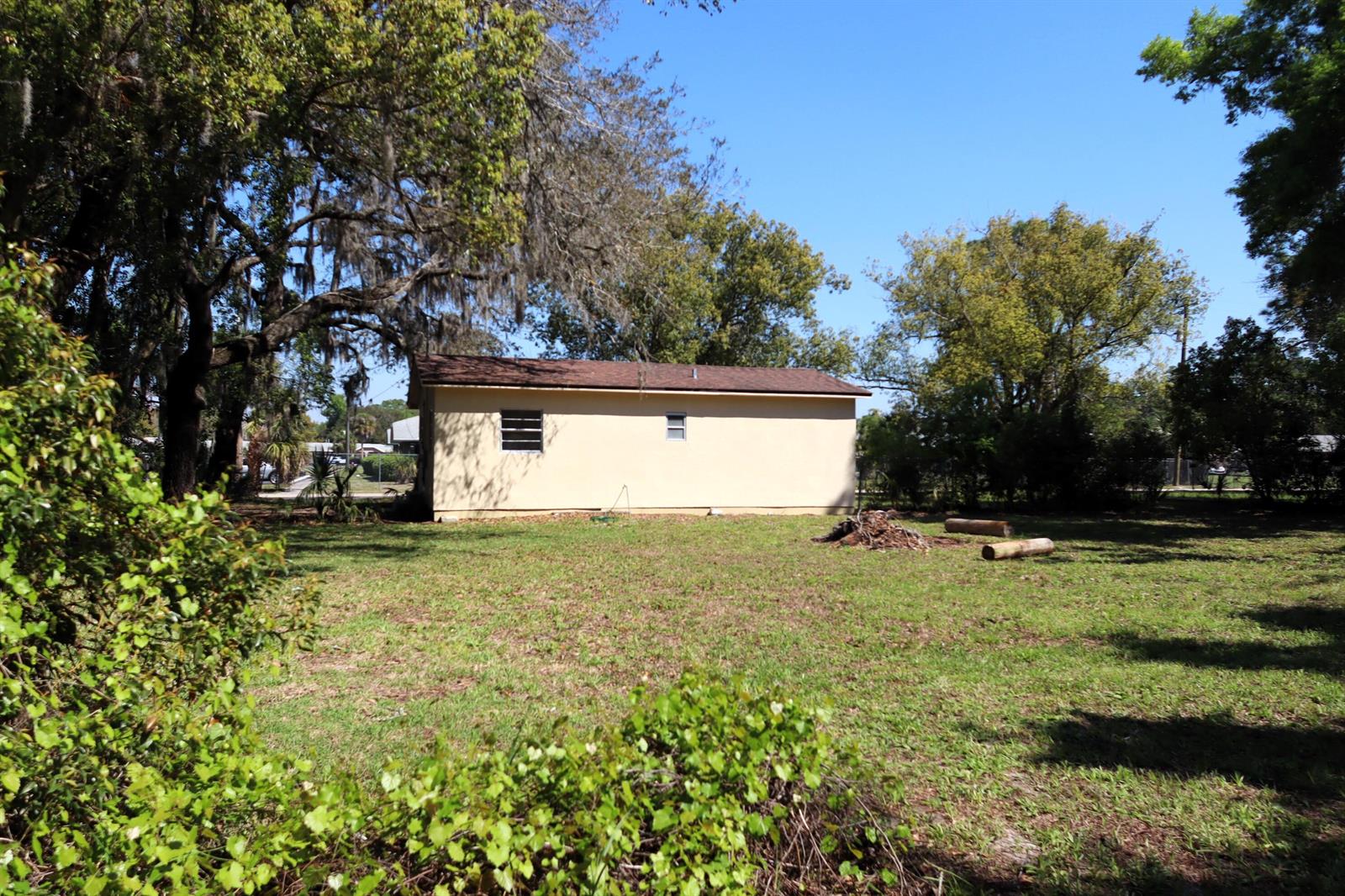A beige, single-story rectangular building sits in a grassy yard surrounded by trees — 2024 Dixie Avenue, FL 32726, FL