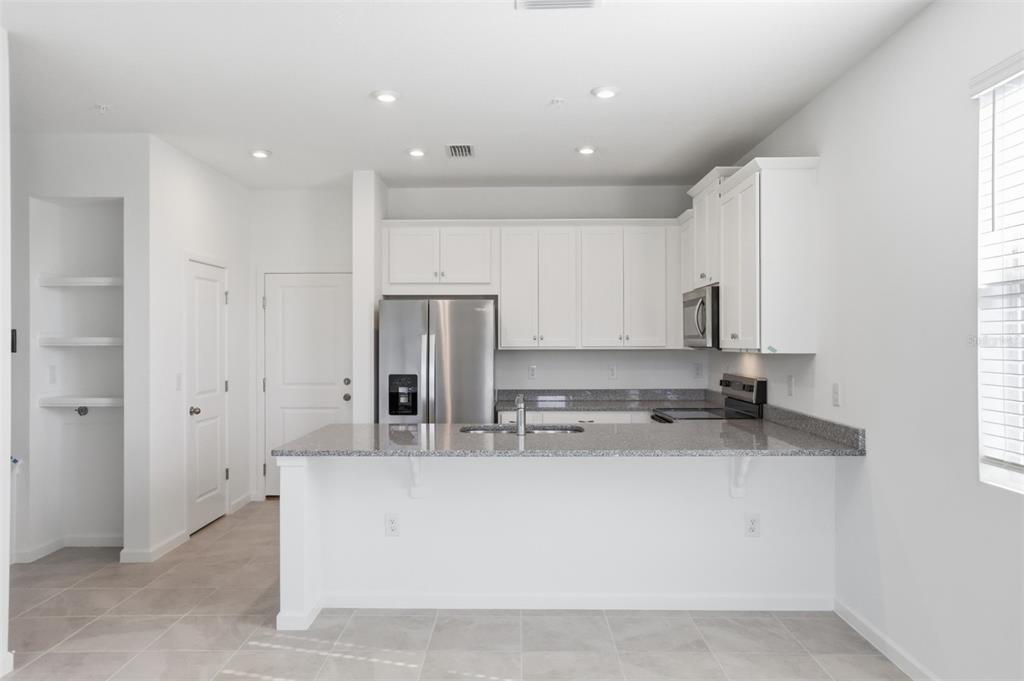 A kitchen features white cabinets, granite countertops, stainless steel appliances, and a breakfast bar — 2199 NIGHTSHADE GROVE LANE, APOPKA, FL