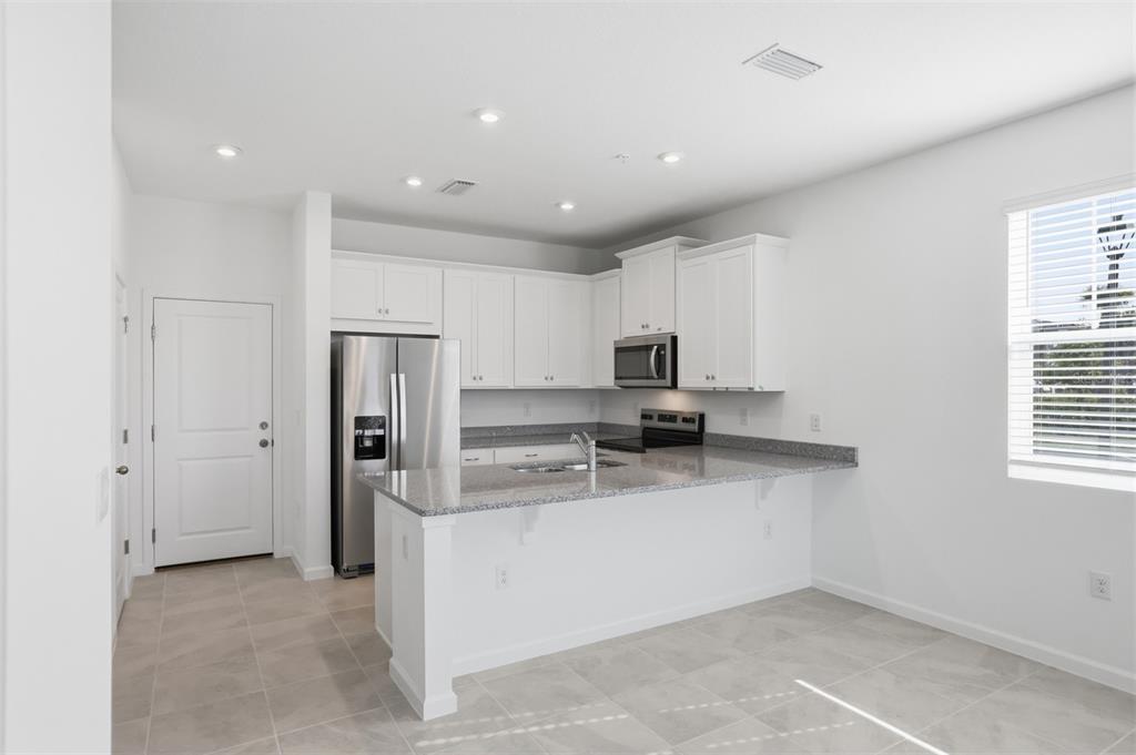 A kitchen with white cabinets, granite countertops, stainless steel appliances, and light tile flooring — 2199 NIGHTSHADE GROVE LANE, APOPKA, FL