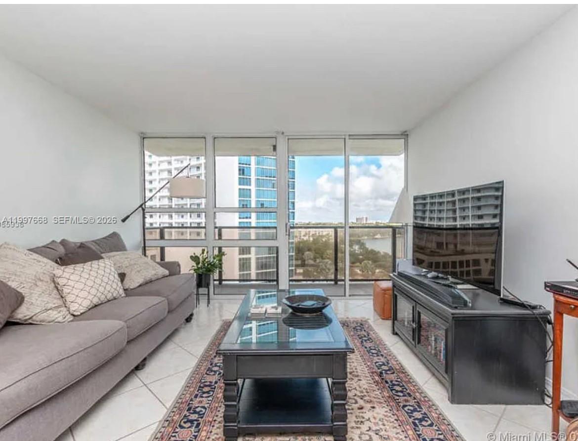 A living room with a gray sofa, glass coffee table, and a balcony overlooking water — 600 NE 36th St # 1006, Miami FL 33137, MIAMI, FL