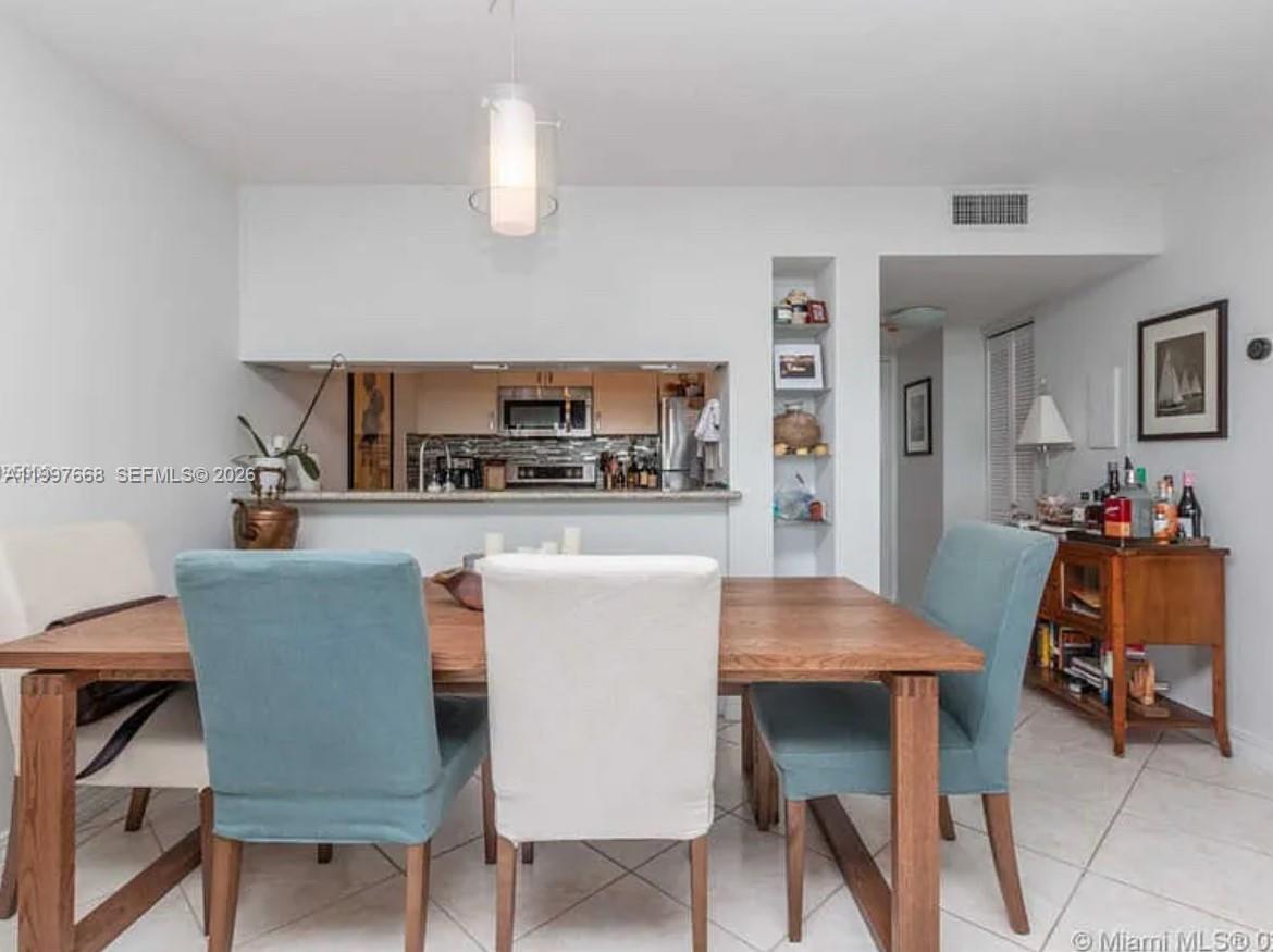 A dining area features a wooden table, upholstered chairs, and an open kitchen pass-through window — 600 NE 36th St # 1006, Miami FL 33137, MIAMI, FL