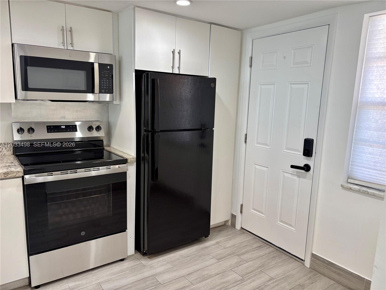 A kitchen features white cabinets, stainless steel appliances, a black refrigerator, and light wood flooring — MIAMI, FL