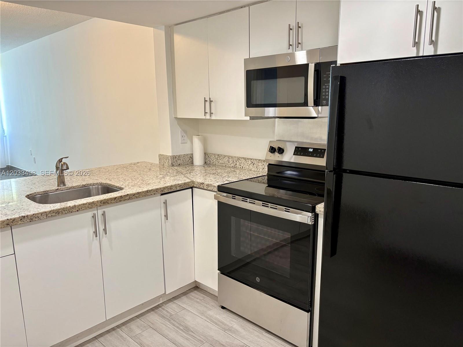 A kitchen features white cabinets, granite countertops, stainless steel appliances, and a black refrigerator — MIAMI, FL