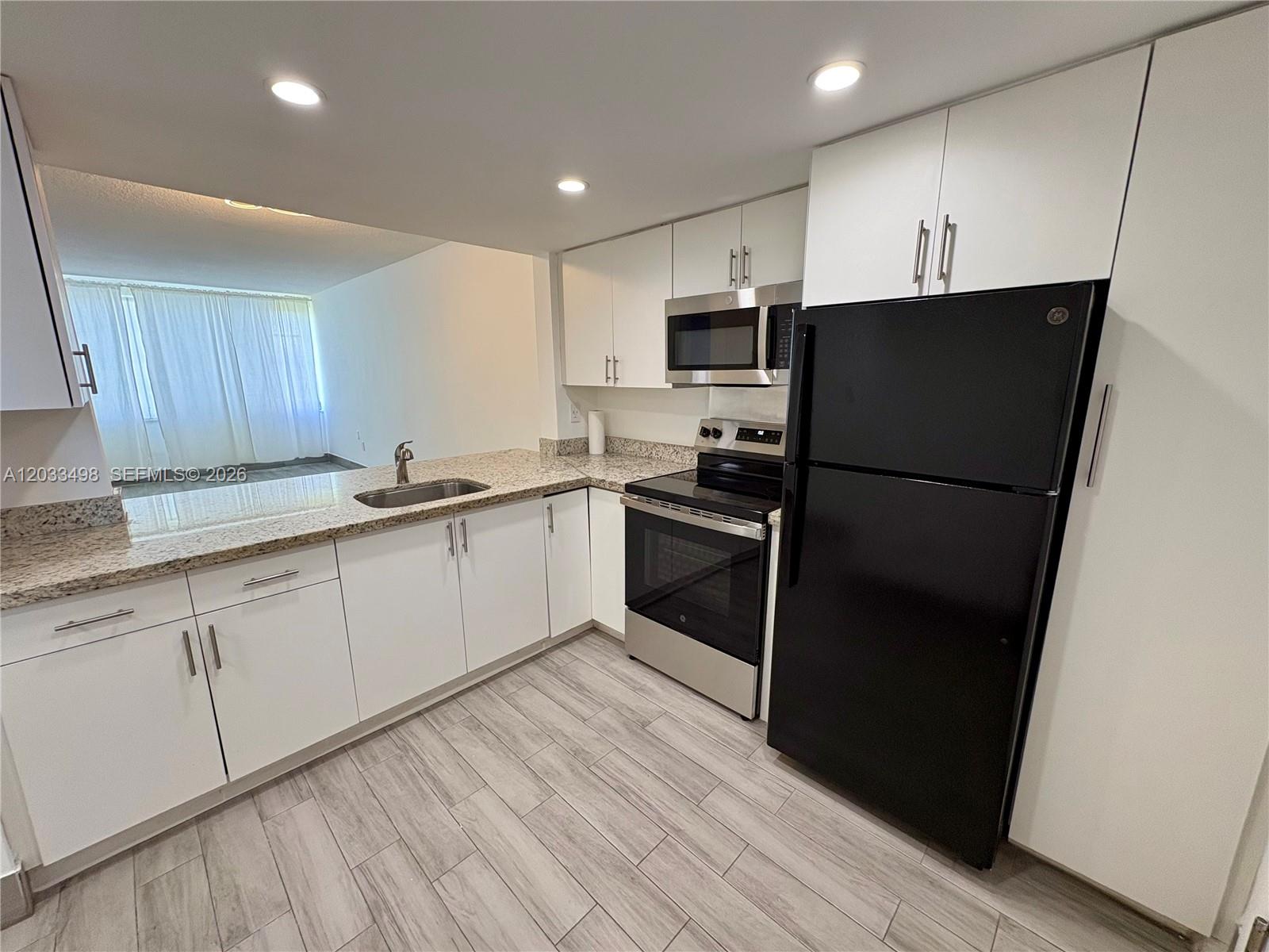 A kitchen features white cabinets, granite countertops, stainless steel appliances, and a black refrigerator — MIAMI, FL