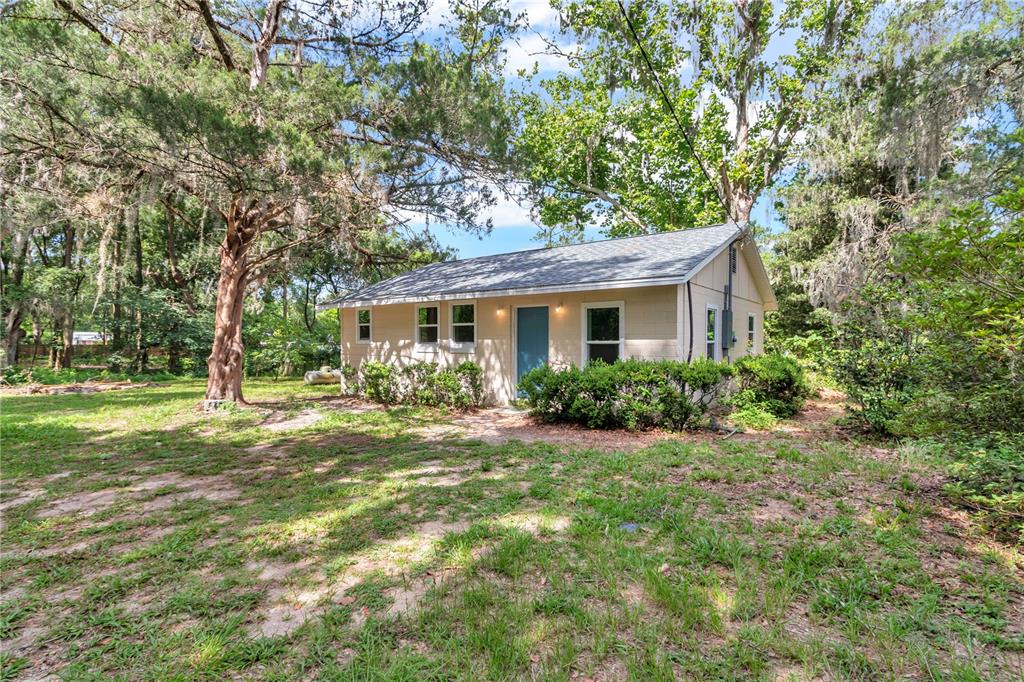 A small, light-colored house with a blue door sits in a grassy, tree-filled yard — 658 NE 39TH COURT, OCALA, FL