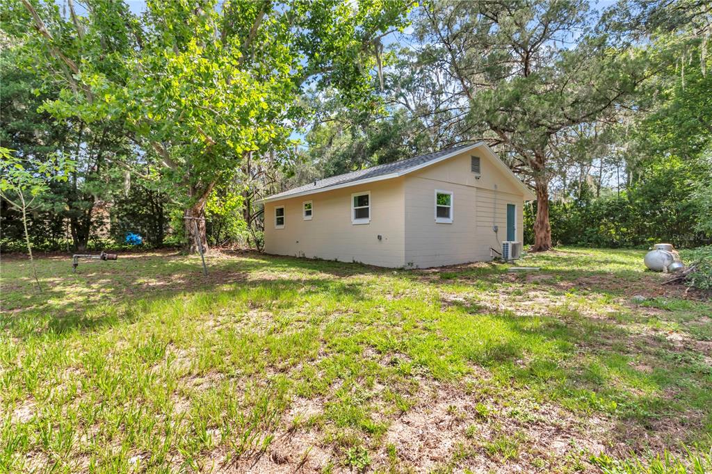 A small, light-colored detached building sits in a grassy yard surrounded by mature trees — 658 NE 39TH COURT, OCALA, FL