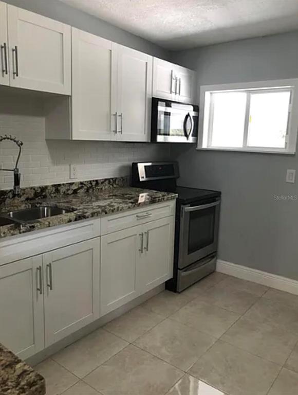 A kitchen features white cabinets, granite countertops, stainless steel appliances, and light-colored tile flooring — 3001 E MCBERRY STREET, TAMPA, FL