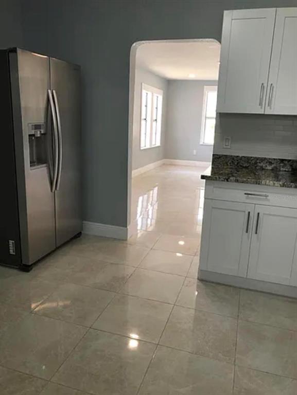 A kitchen with stainless steel refrigerator, white cabinets, granite countertops, and light-colored tile flooring — 3001 E MCBERRY STREET, TAMPA, FL