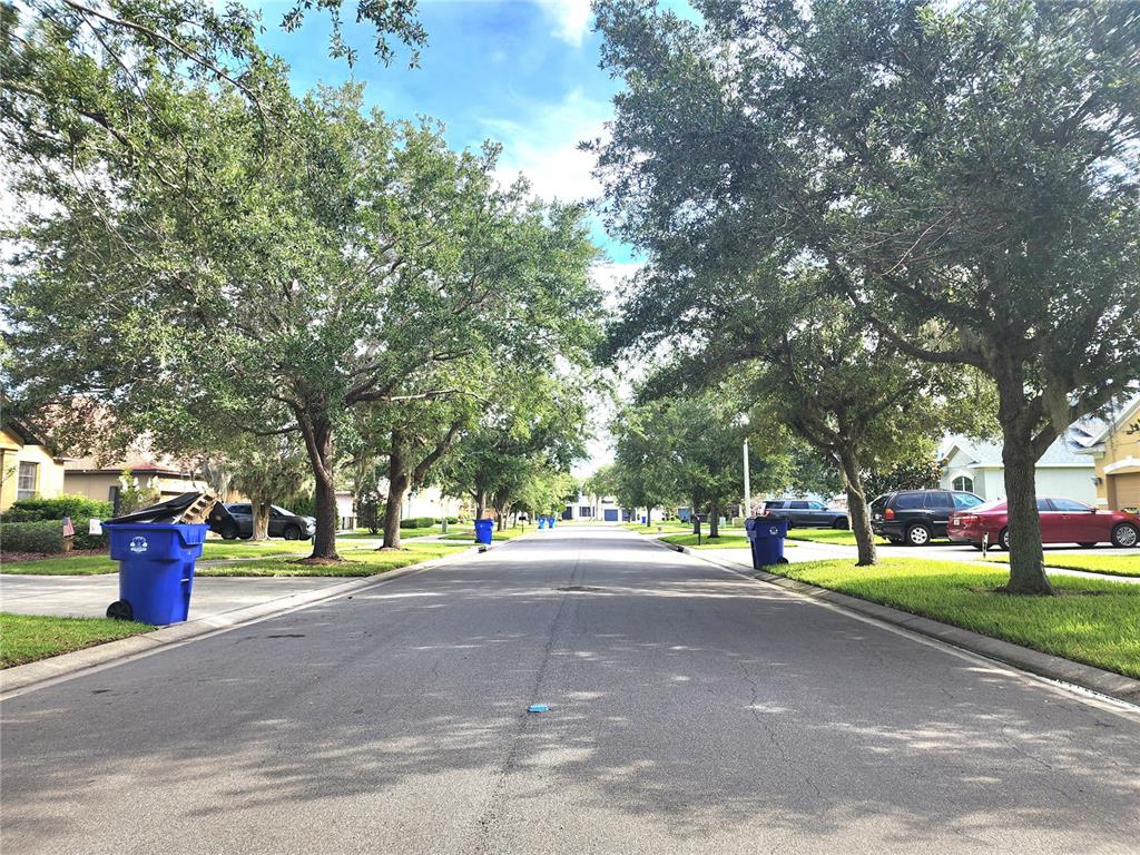 A suburban residential street lined with mature trees, parked cars, and blue trash bins — 4061 ASHEVILLE LANE, ST CLOUD, FL