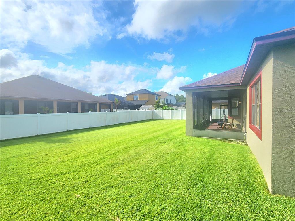 A grassy backyard features a white vinyl fence and a screened-in patio attached to a house — 4061 ASHEVILLE LANE, ST CLOUD, FL