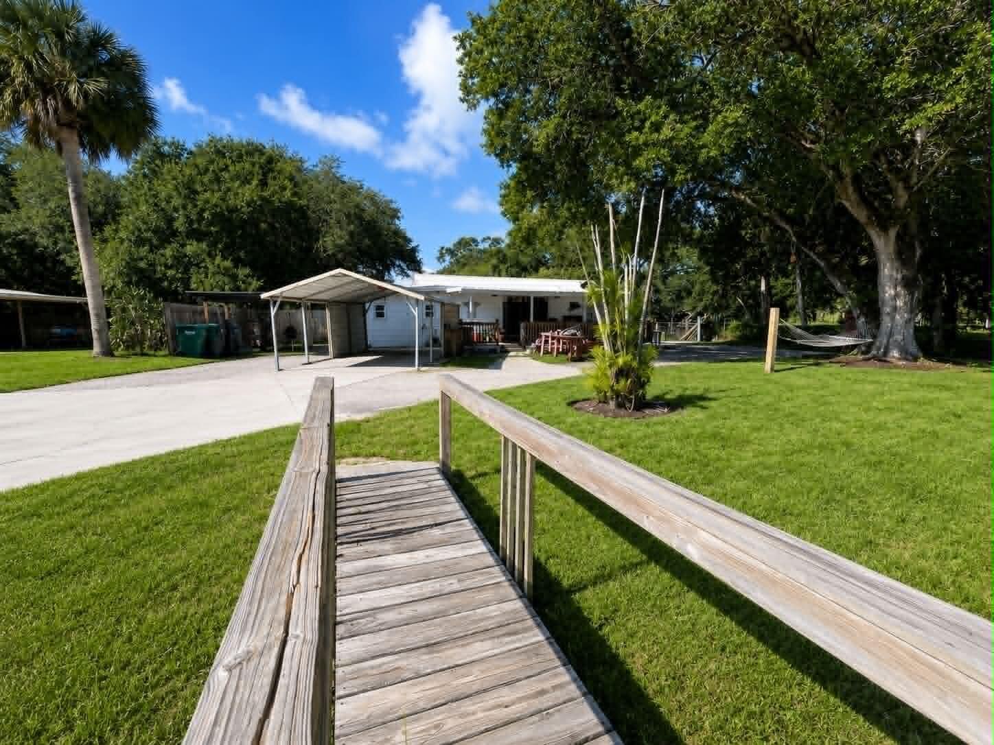 A wooden footbridge leads across a lawn toward a house with a carport — 1111 NW 3rd Street, Okeechobee FL 34972, OKEECHOBEE, FL