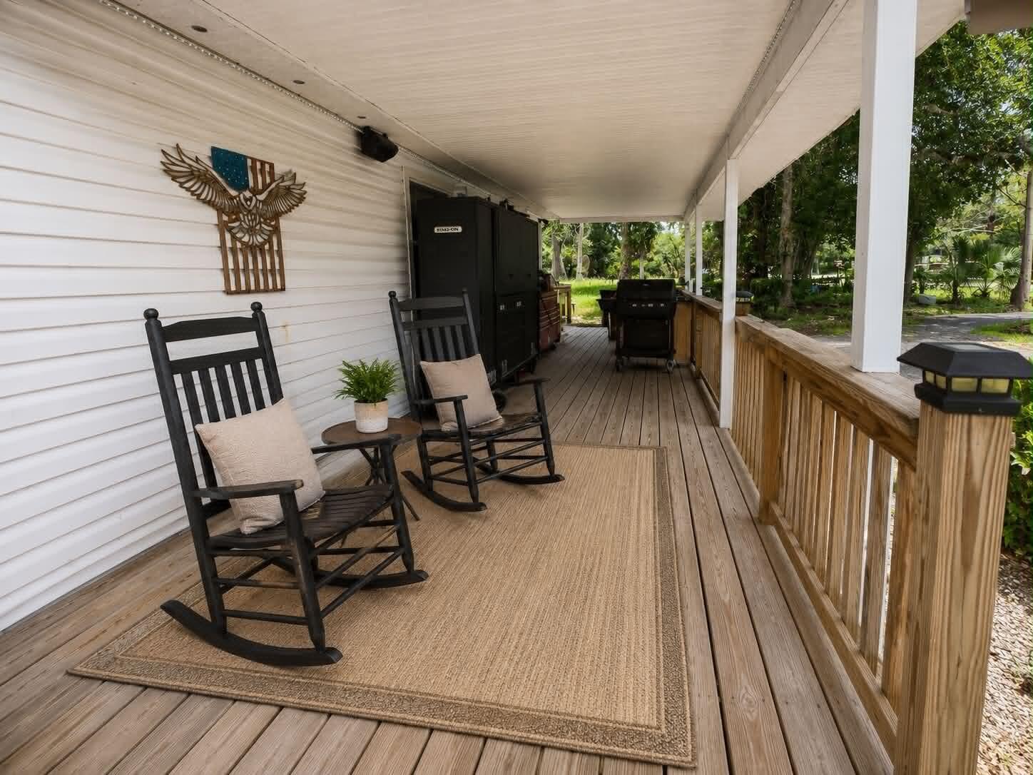 A covered wooden porch features two black rocking chairs, a small table, and a rug — 1111 NW 3rd Street, Okeechobee FL 34972, OKEECHOBEE, FL