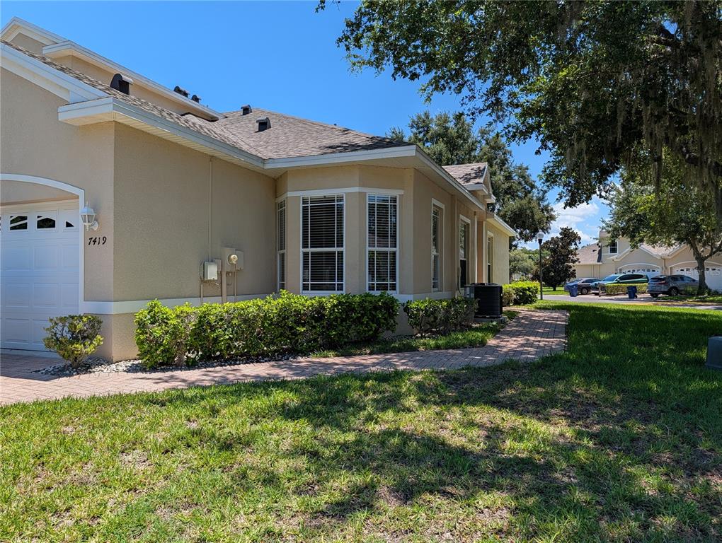 A tan house exterior features a brick walkway, a garage, and a bay window — 7419 WIMPOLE DRIVE, NEW PORT RICHEY, FL