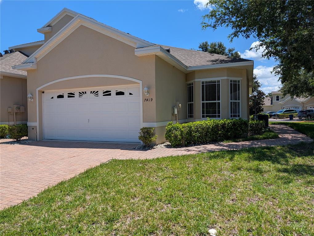 A tan house exterior features a two-car garage, a bay window, and a brick driveway — 7419 WIMPOLE DRIVE, NEW PORT RICHEY, FL