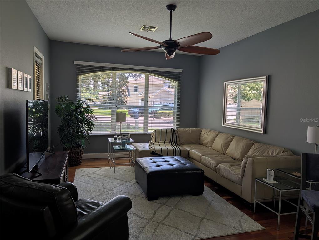 A living room features a sectional sofa, leather ottoman, ceiling fan, and large windows — 7419 WIMPOLE DRIVE, NEW PORT RICHEY, FL