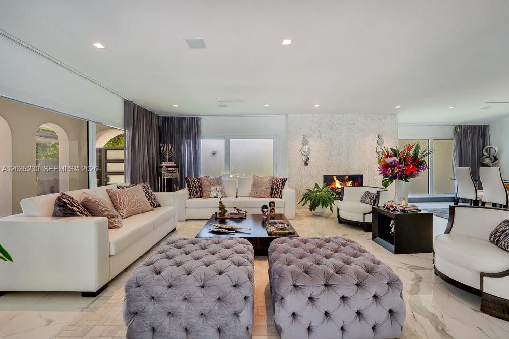 A bright living room features white sofas, tufted ottomans, a fireplace, and marble flooring — 6460 SW 133rd Dr, Pinecrest FL 33156, PINECREST, FL