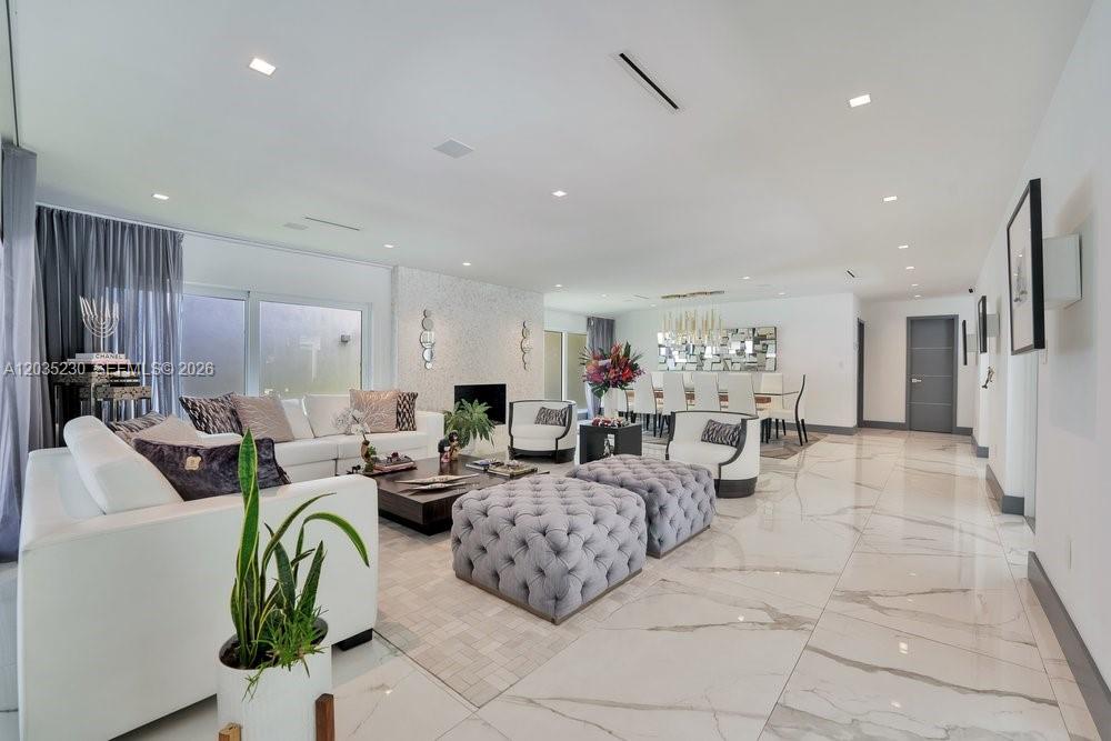 A spacious living and dining area features white tile floors, tufted ottomans, and modern furniture — 6460 SW 133rd Dr, Pinecrest FL 33156, PINECREST, FL